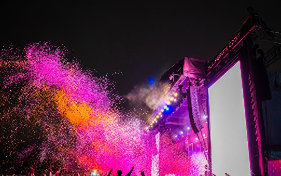 A photograph of Bombay Bicycle Club playing at All Points East at night. Colourful clouds fill the air