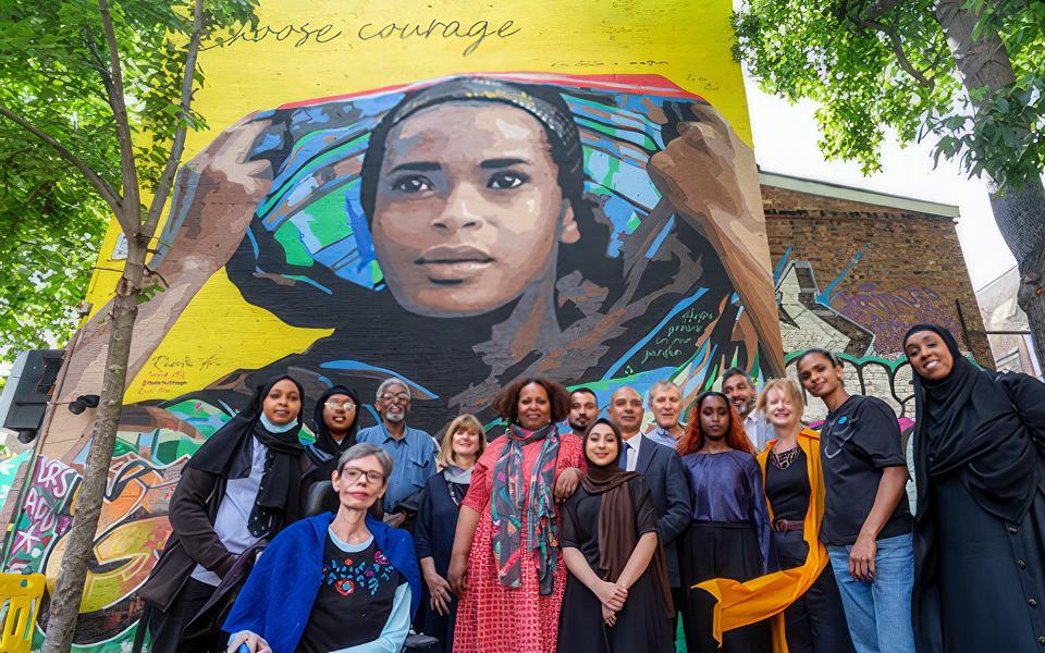 Photo of a diverse group of people in front of the Choose Courage mural of boxer Ramla Ali
