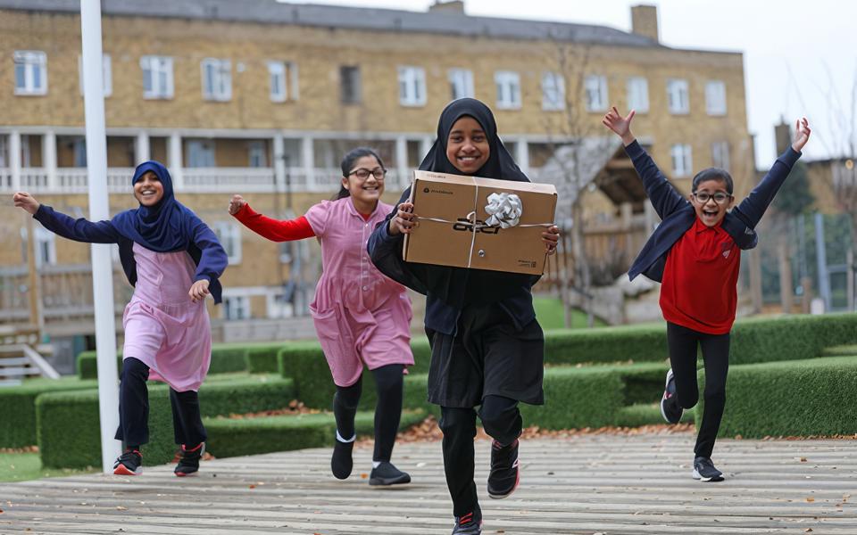 A child and her friends celebrating receiving a new, boxed laptop, running towards the camera